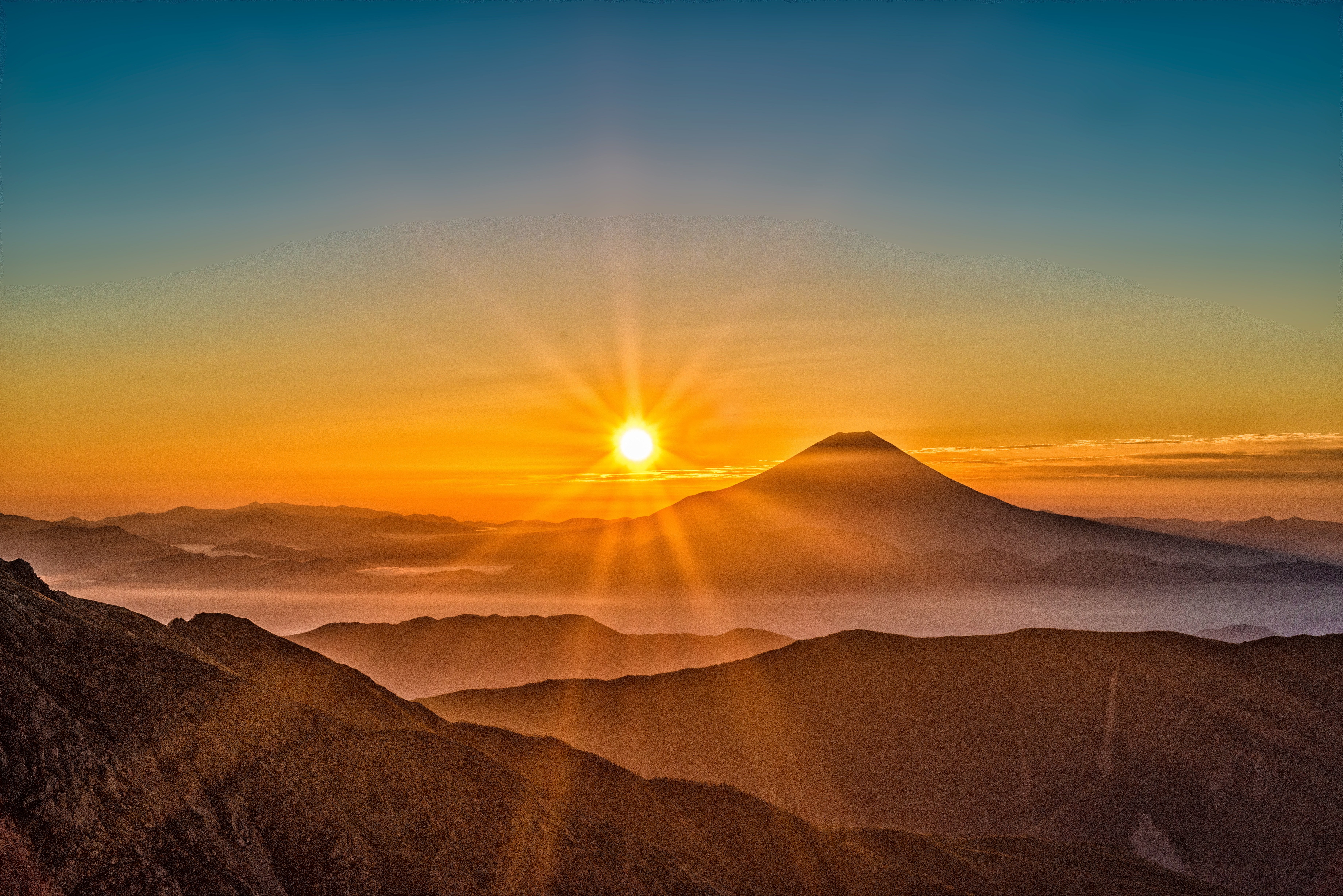 Mount Fuji im warmen Licht eines Sonnenaufgangs über mehreren Bergketten